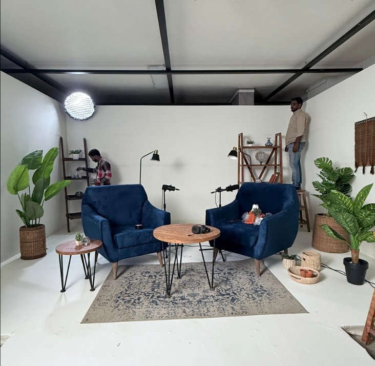 The same studio after set design, with blue armchairs, a round table, plants and warm lamps